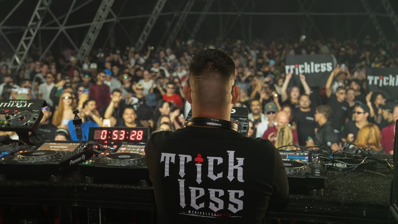 TrickLess de costas para a pista lotada da final do Circuito no Park Art, camiseta Trick less, CDJs Pioneer e o público com placas do nome.